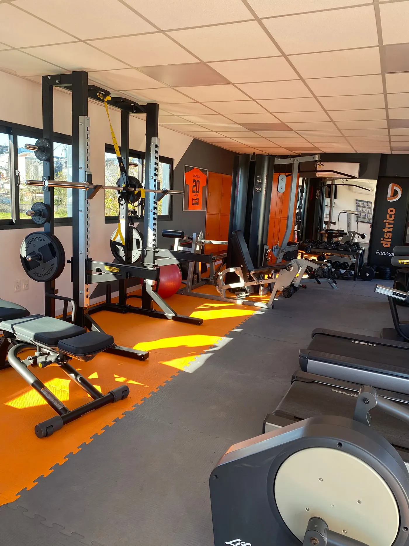 Gimnasio de DISTRICO con racks de pesas, máquinas y el cartel de Districo Fitness